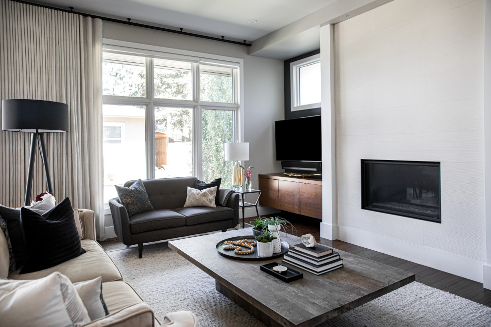 Großes, Offenes Modernes Wohnzimmer mit grauer Wandfarbe, braunem Holzboden, Kamin, gefliester Kaminumrandung, freistehendem TV und braunem Boden in Calgary