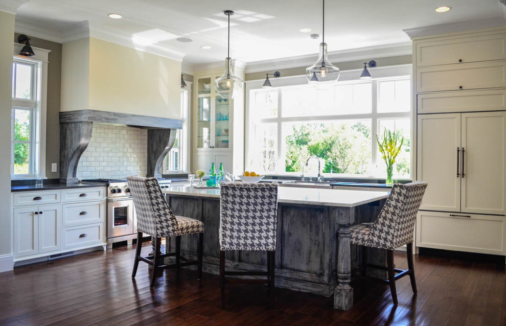 Example of a transitional l-shaped dark wood floor eat-in kitchen design with a farmhouse sink, flat-panel cabinets, white cabinets, marble countertops, white backsplash, subway tile backsplash, paneled appliances and an island