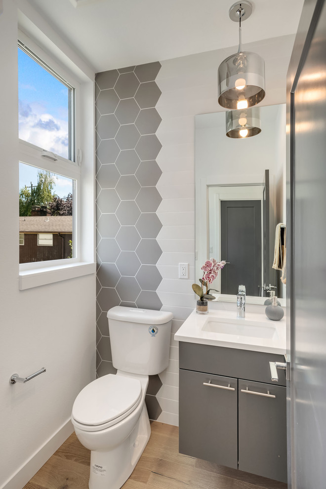 Photo of a contemporary powder room in Seattle with flat-panel cabinets, grey cabinets, gray tile, white walls, medium hardwood floors, an undermount sink, brown floor and white benchtops.