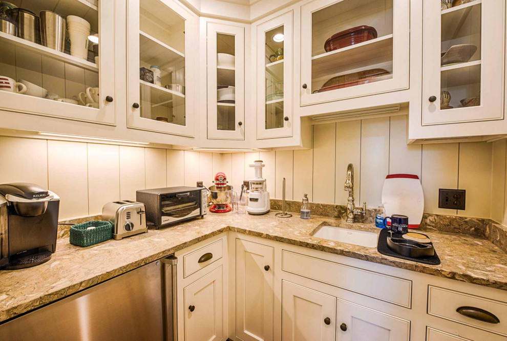 L-shaped kitchen pantry photo with an undermount sink, beaded inset cabinets, white cabinets, limestone countertops, beige backsplash, limestone backsplash, stainless steel appliances and beige countertops