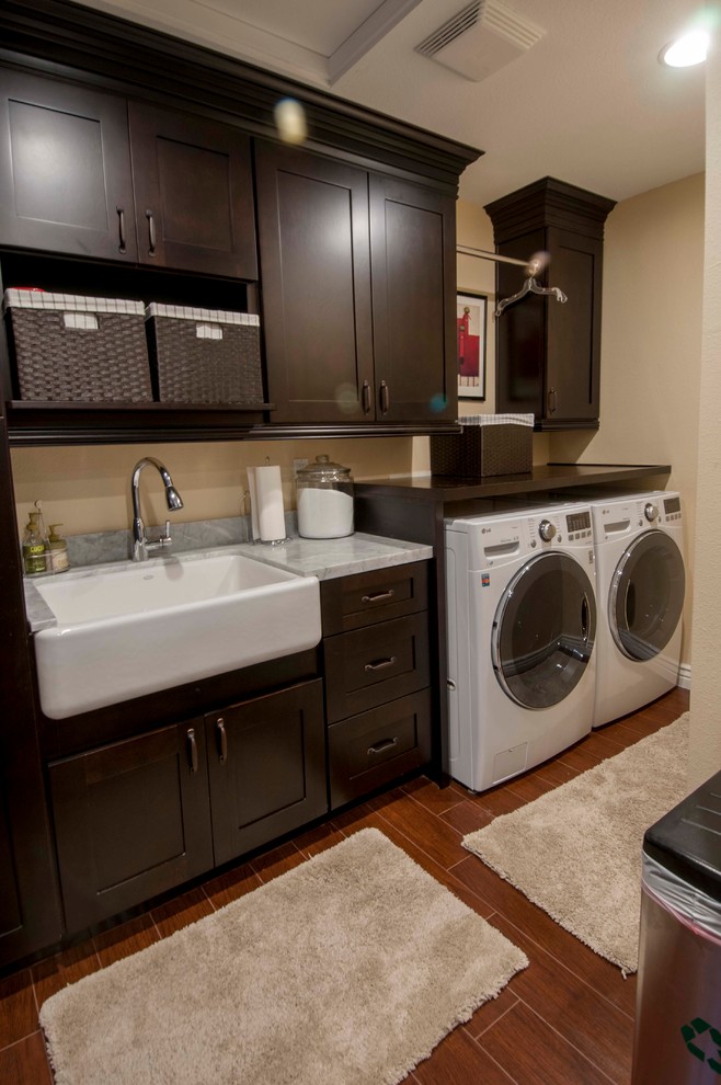 Design ideas for a mid-sized transitional single-wall utility room in Phoenix with a farmhouse sink, flat-panel cabinets, dark wood cabinets, limestone benchtops, yellow walls, medium hardwood floors and a side-by-side washer and dryer.