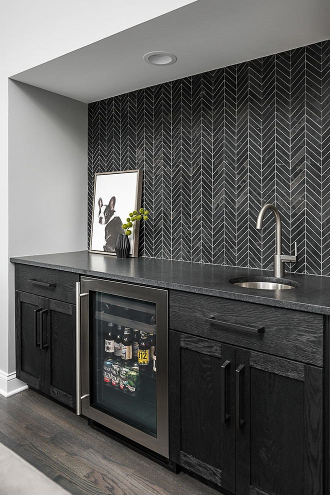 Design ideas for a mid-sized transitional single-wall wet bar in Chicago with an undermount sink, black cabinets, black splashback, black benchtop, dark hardwood floors, shaker cabinets, soapstone benchtops and brown floor.