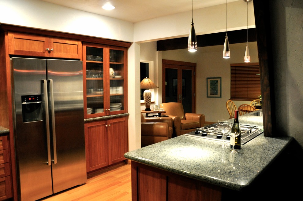 Example of a mid-sized transitional l-shaped medium tone wood floor and brown floor eat-in kitchen design with a farmhouse sink, shaker cabinets, medium tone wood cabinets, granite countertops, green backsplash, stone slab backsplash, stainless steel appliances and a peninsula