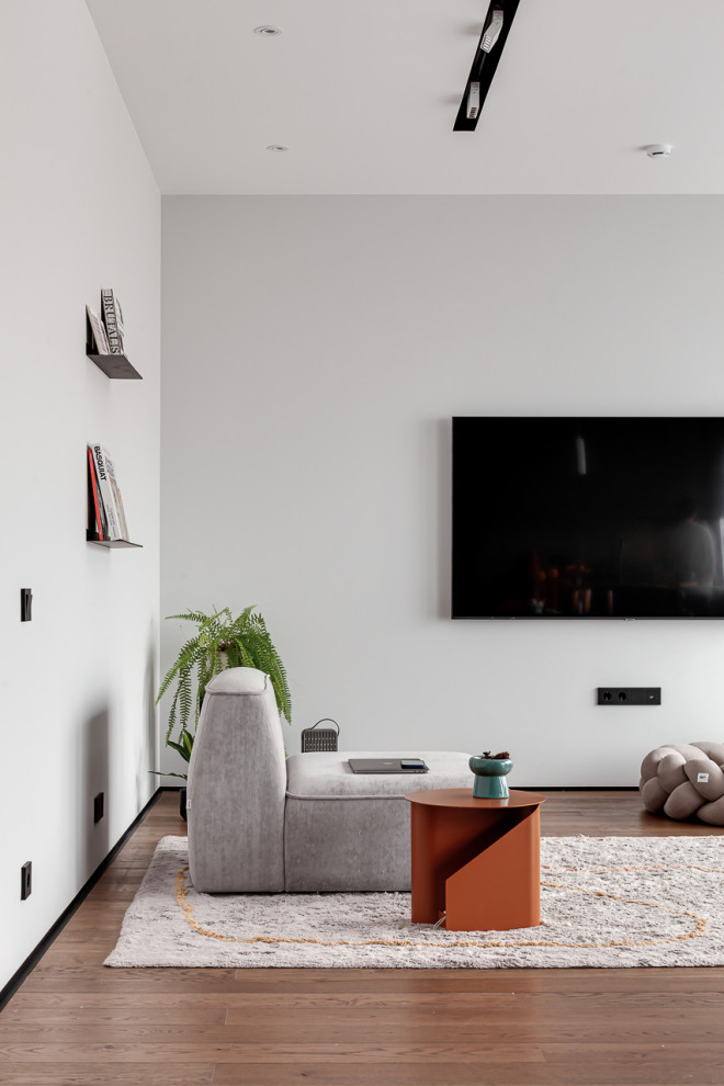 Идея дизайна: огромная объединенная, серо-белая гостиная комната в современном стиле с с книжными шкафами и полками, белыми стенами, паркетным полом среднего тона, телевизором на стене, зоной отдыха и коричневым полом