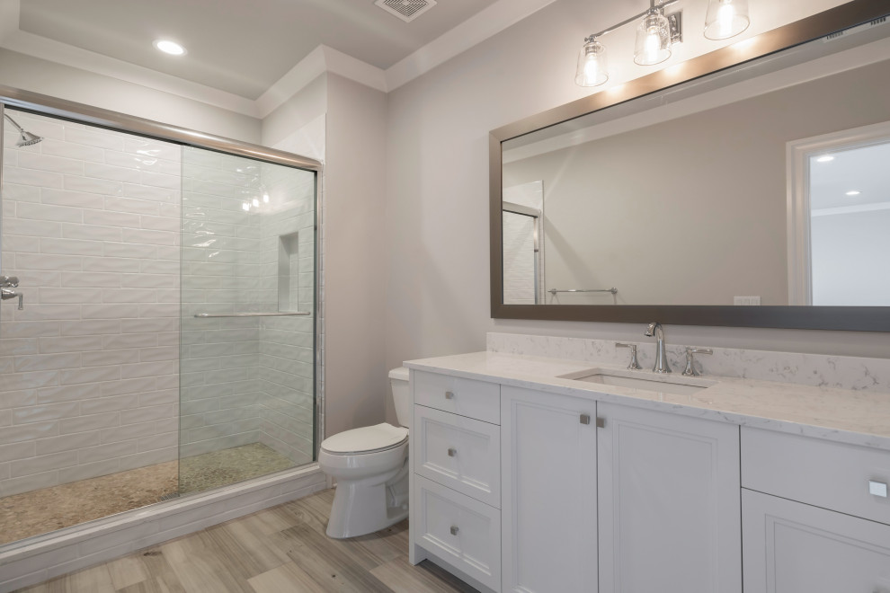 This is an example of a mid-sized transitional kids bathroom in Atlanta with furniture-like cabinets, white cabinets, a two-piece toilet, white tile, porcelain tile, grey walls, porcelain floors, an undermount sink, engineered quartz benchtops, grey floor, a sliding shower screen and white benchtops.