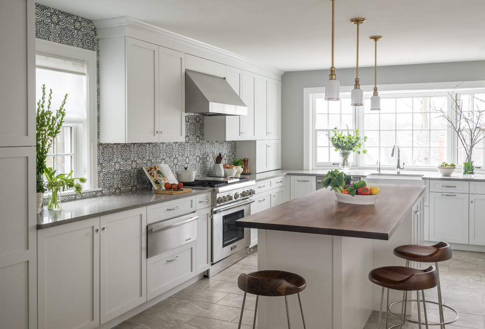This is an example of a transitional u-shaped separate kitchen in Boston with a farmhouse sink, shaker cabinets, white cabinets, stainless steel appliances, with island, grey floor, wood benchtops, multi-coloured splashback and ceramic splashback.