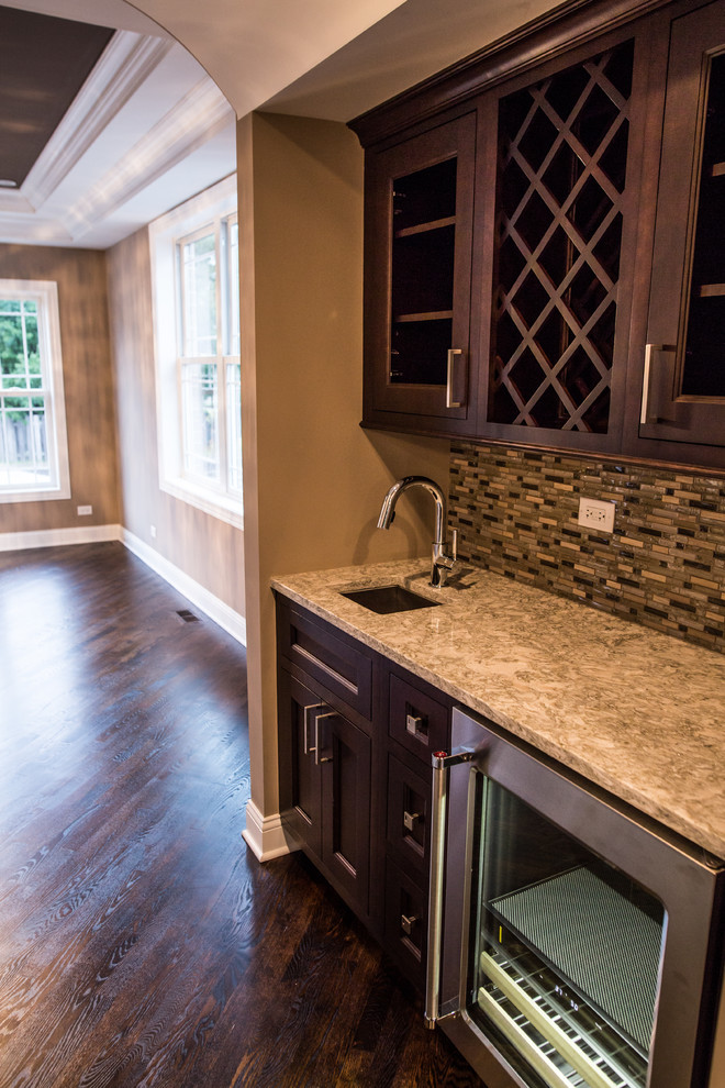 Inspiration for a mid-sized transitional l-shaped dark wood floor home design remodel in Chicago with an undermount sink, shaker cabinets, brown cabinets, granite countertops, gray backsplash, subway tile backsplash, stainless steel appliances and an island