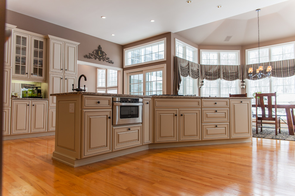 Inspiration for an expansive traditional u-shaped eat-in kitchen in New York with an undermount sink, raised-panel cabinets, beige cabinets, granite benchtops, beige splashback, terra-cotta splashback, panelled appliances, light hardwood floors and with island.