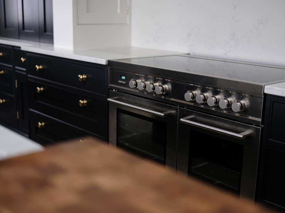 Photo of a classic kitchen in Cheshire with a belfast sink, black cabinets, quartz worktops, an island and white worktops.