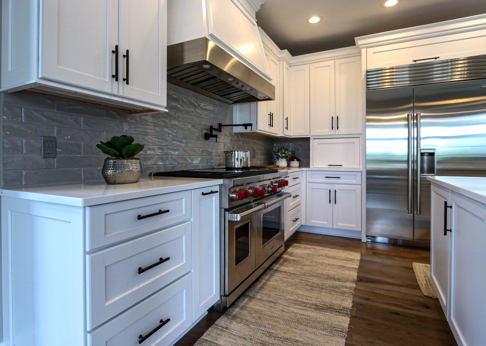 クリーブランドにある高級な広いトランジショナルスタイルのおしゃれなキッチン (アンダーカウンターシンク、フラットパネル扉のキャビネット、白いキャビネット、クオーツストーンカウンター、グレーのキッチンパネル、ガラスタイルのキッチンパネル、シルバーの調理設備、無垢フローリング、ベージュの床、白いキッチンカウンター) の写真