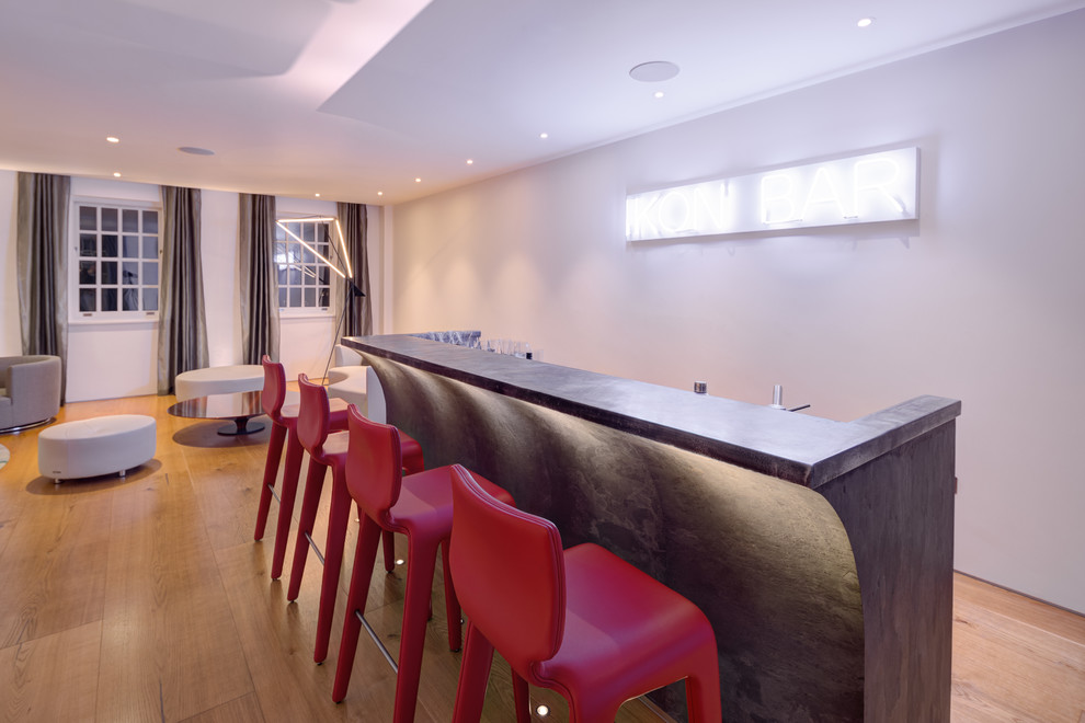 Large modern single-wall wet bar in London with a drop-in sink, flat-panel cabinets, grey cabinets, zinc benchtops, black splashback and light hardwood floors.