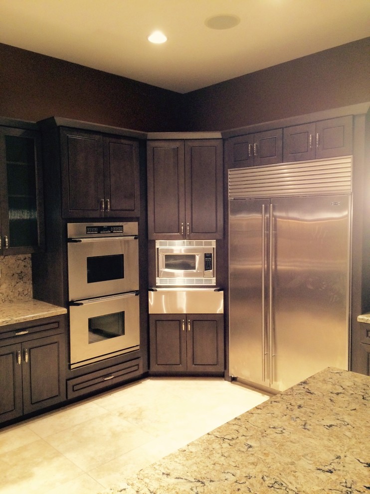 Large transitional l-shaped ceramic tile and beige floor kitchen photo in Phoenix with a double-bowl sink, raised-panel cabinets, dark wood cabinets, granite countertops, multicolored backsplash, stone slab backsplash, stainless steel appliances and an island