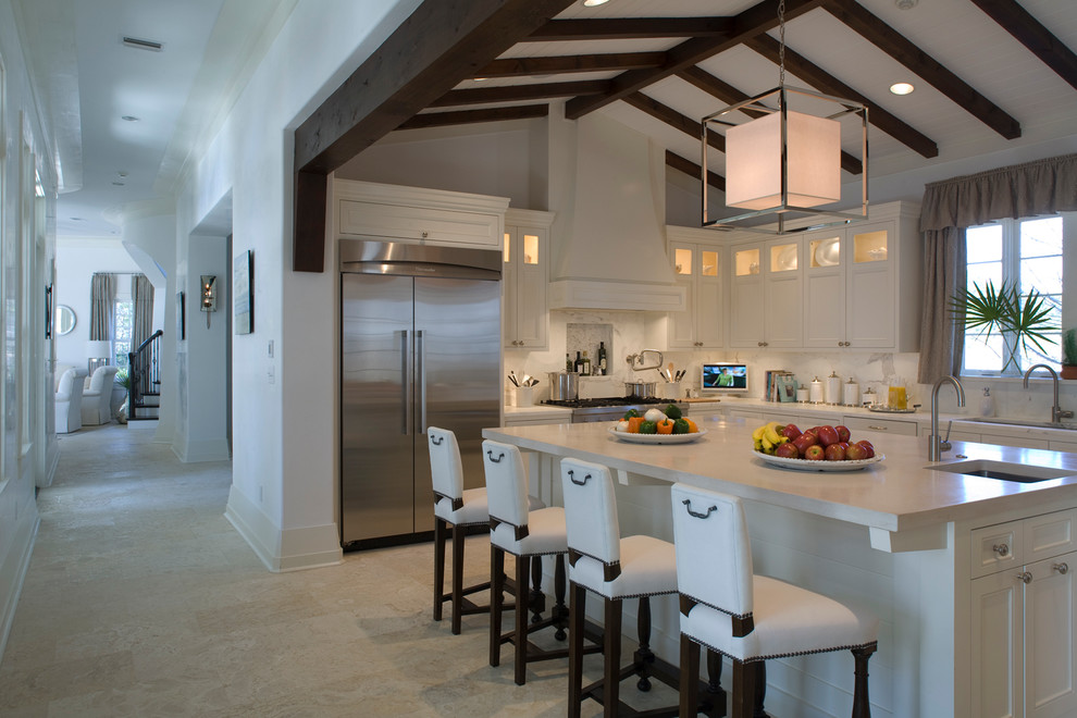Photo of a large mediterranean l-shaped eat-in kitchen in Miami with an undermount sink, shaker cabinets, white cabinets, marble benchtops, white splashback, stone slab splashback, stainless steel appliances, limestone floors and with island.