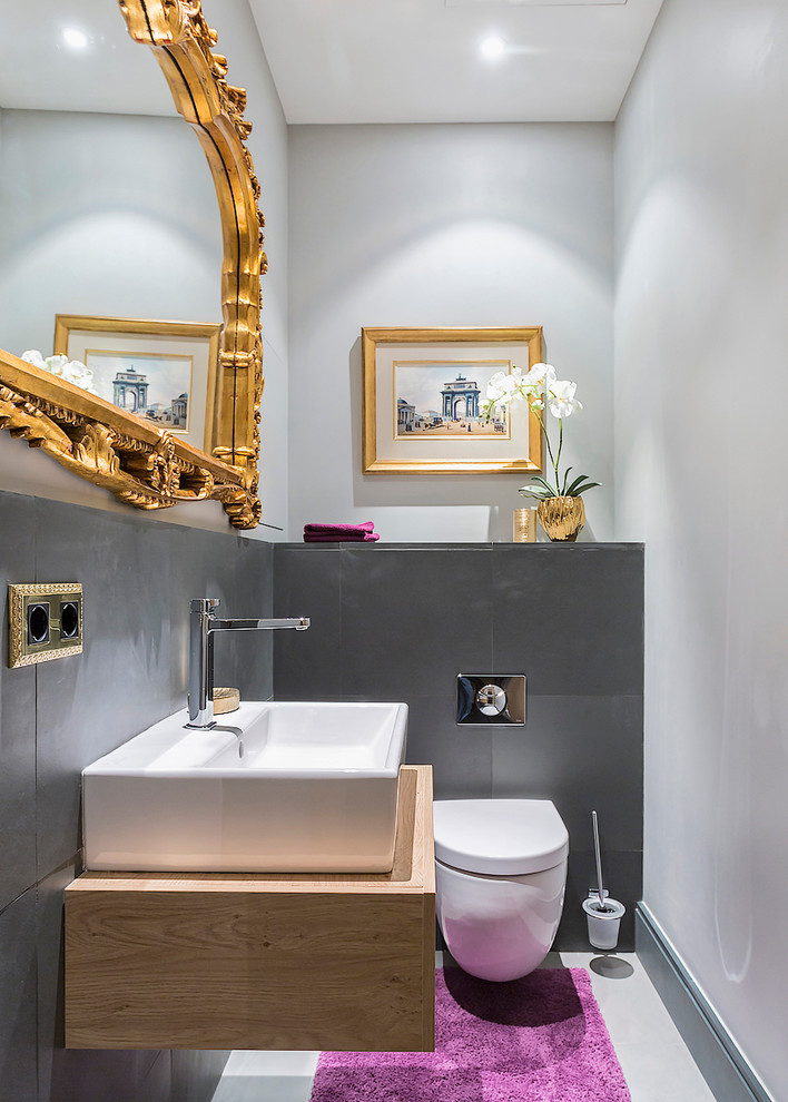 Contemporary powder room in Moscow with flat-panel cabinets, light wood cabinets, a wall-mount toilet, a vessel sink and grey walls.