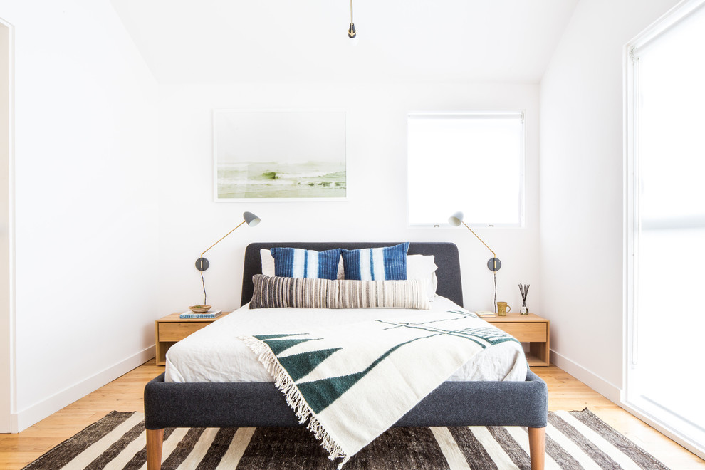 Scandinavian master bedroom in Los Angeles with white walls, light hardwood floors and brown floor.