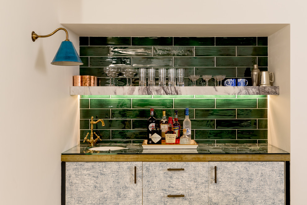 Large eclectic single-wall wet bar in London with an undermount sink, flat-panel cabinets, grey cabinets, glass benchtops, green splashback and subway tile splashback.