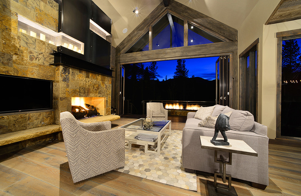 Photo of a large country open concept living room in Denver with beige walls, medium hardwood floors, a standard fireplace, a stone fireplace surround, a wall-mounted tv and brown floor.