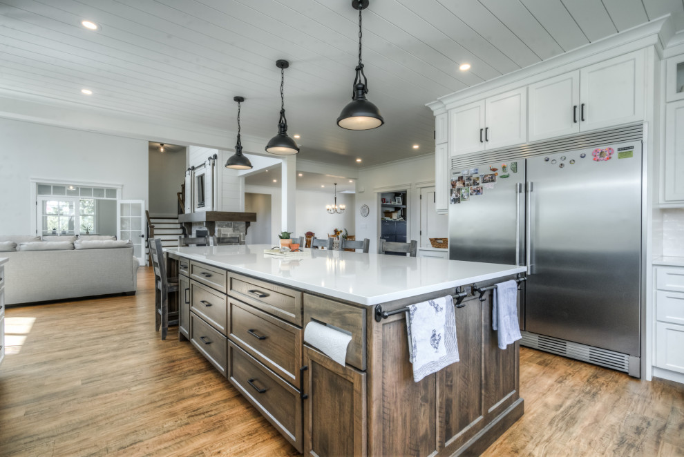 Photo of a large country u-shaped kitchen in Toronto with a farmhouse sink, shaker cabinets, white cabinets, quartz benchtops, white splashback, cement tile splashback, stainless steel appliances, medium hardwood floors, with island, multi-coloured floor, white benchtop and timber.