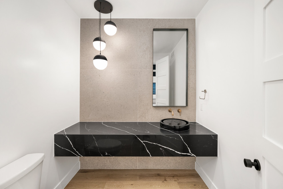 Photo of an industrial cloakroom in Denver with black cabinets, a two-piece toilet, grey tiles, cement tiles, white walls, light hardwood flooring, a vessel sink, quartz worktops, brown floors, beige worktops and a floating vanity unit.