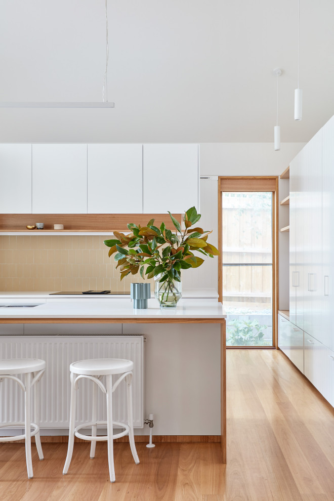 Photo of a contemporary l-shaped open plan kitchen in Melbourne with a double-bowl sink, flat-panel cabinets, white cabinets, quartz benchtops, beige splashback, ceramic splashback, stainless steel appliances, light hardwood floors, with island, brown floor and white benchtop.