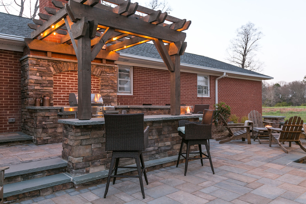 Photo of a mid-sized country backyard patio in Charlotte with an outdoor kitchen, concrete pavers and a pergola.