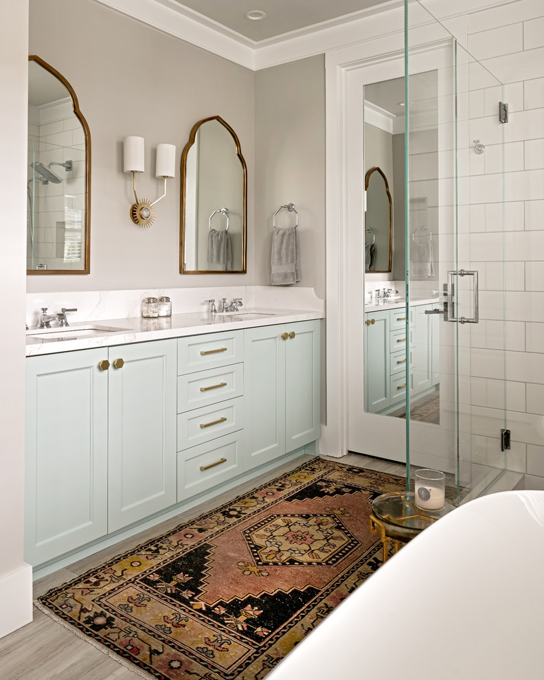This is an example of a mid-sized transitional master bathroom in Charlotte with recessed-panel cabinets, turquoise cabinets, a freestanding tub, a corner shower, white tile, ceramic tile, grey walls, porcelain floors, an undermount sink, engineered quartz benchtops, grey floor, a hinged shower door, white benchtops, a bidet, an enclosed toilet, a double vanity, a built-in vanity and decorative wall panelling.