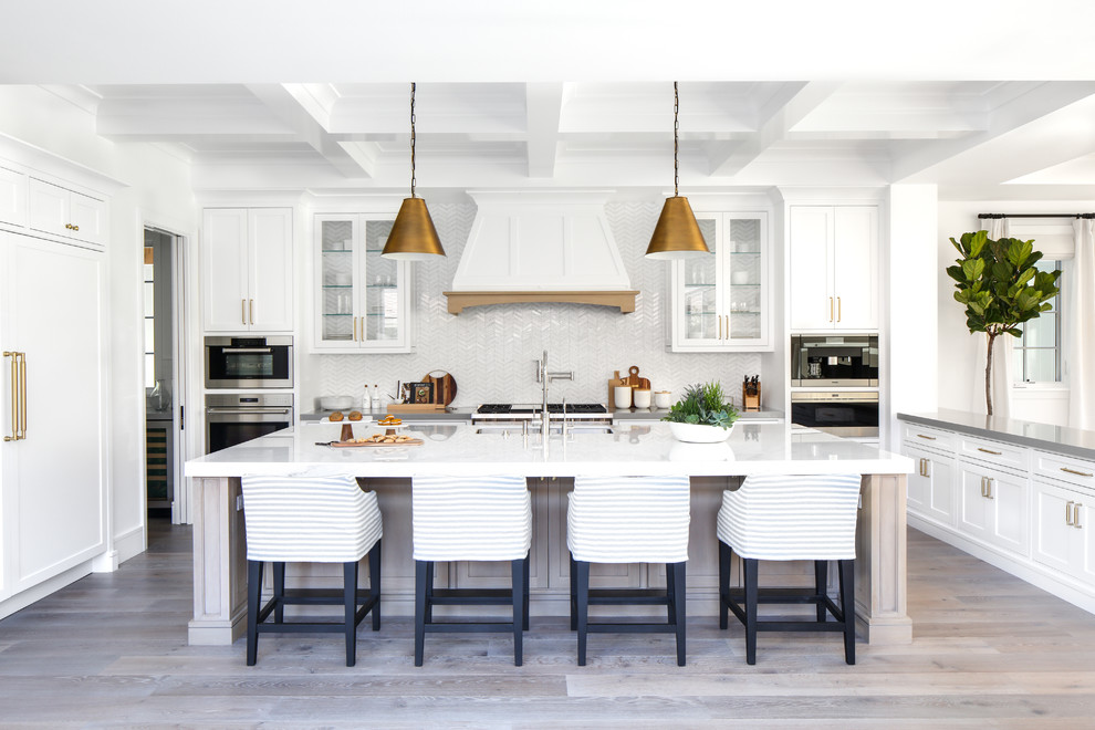 Large modern u-shaped open plan kitchen in Orange County with white cabinets, solid surface benchtops, white splashback, stainless steel appliances, with island, medium hardwood floors, grey floor and beaded inset cabinets.
