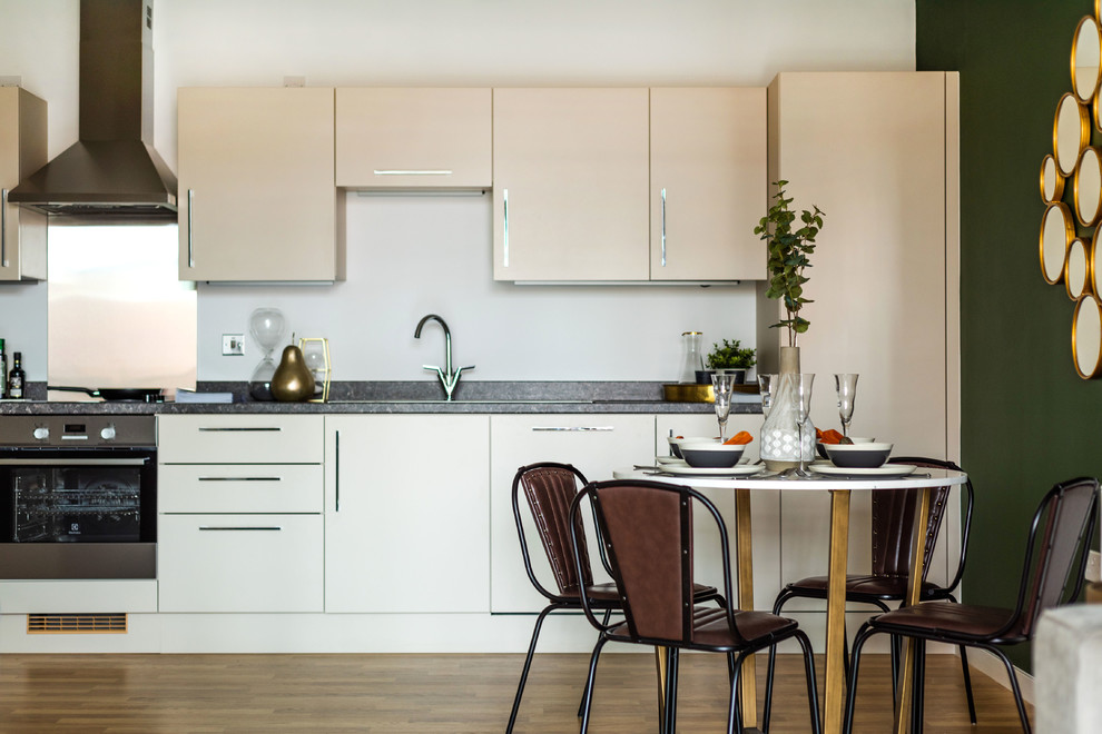 This is an example of a contemporary single-wall open plan kitchen in London with flat-panel cabinets, white cabinets, stainless steel appliances, medium hardwood floors, no island, brown floor and grey benchtop.