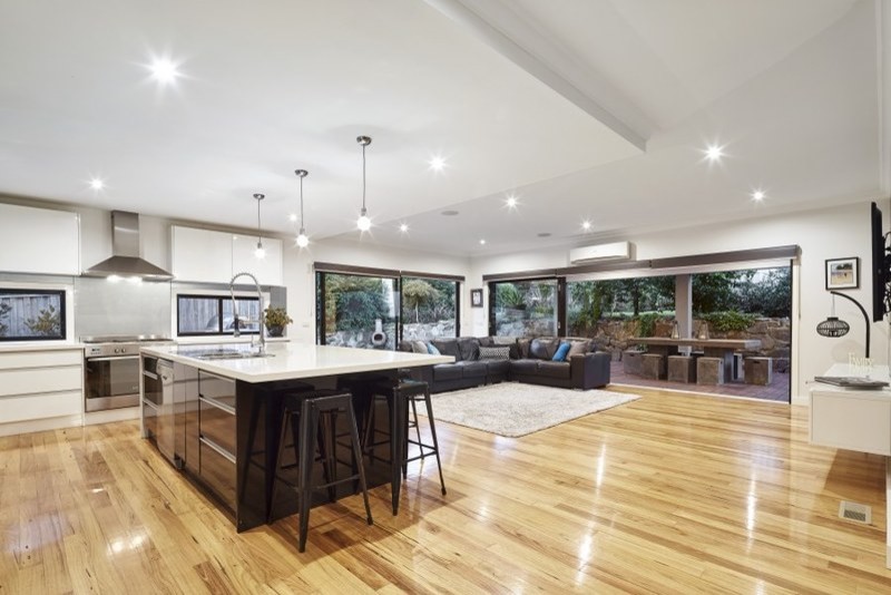 Inspiration for a mid-sized modern l-shaped open plan kitchen in Melbourne with a double-bowl sink, recessed-panel cabinets, black cabinets, glass sheet splashback, stainless steel appliances, medium hardwood floors, with island, quartz benchtops, white splashback and brown floor.