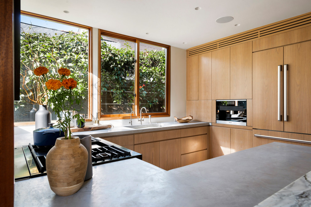 Foto på ett avskilt, litet funkis grå u-kök, med en undermonterad diskho, granitbänkskiva, fönster som stänkskydd, rostfria vitvaror, en halv köksö, brunt golv, släta luckor och skåp i mellenmörkt trä