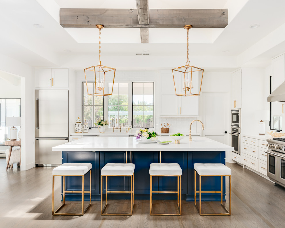 Design ideas for a large country u-shaped eat-in kitchen in San Francisco with a farmhouse sink, shaker cabinets, blue cabinets, quartz benchtops, white splashback, ceramic splashback, stainless steel appliances, light hardwood floors, with island, grey floor and white benchtop.