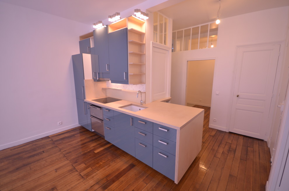 Photo of a mid-sized modern single-wall open plan kitchen in Paris with a single-bowl sink, beaded inset cabinets, blue cabinets, white splashback, mosaic tile splashback, stainless steel appliances, light hardwood floors, no island and beige floor.