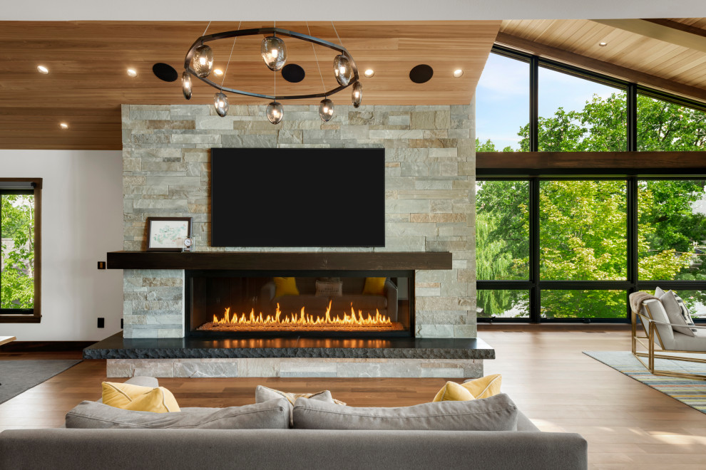This is an example of a large modern open concept living room in Minneapolis with beige walls, medium hardwood floors, a ribbon fireplace, a stone fireplace surround, a wall-mounted tv, brown floor and vaulted.