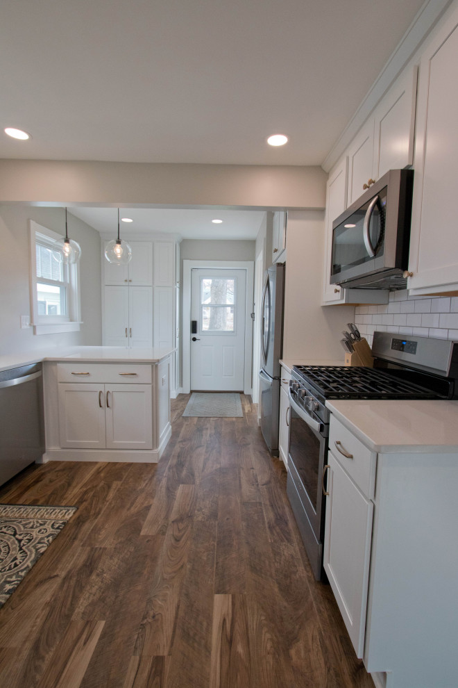 Enclosed kitchen - mid-sized rustic galley vinyl floor and brown floor enclosed kitchen idea with recessed-panel cabinets, white cabinets, quartz countertops, white backsplash, subway tile backsplash, stainless steel appliances, a peninsula and white countertops