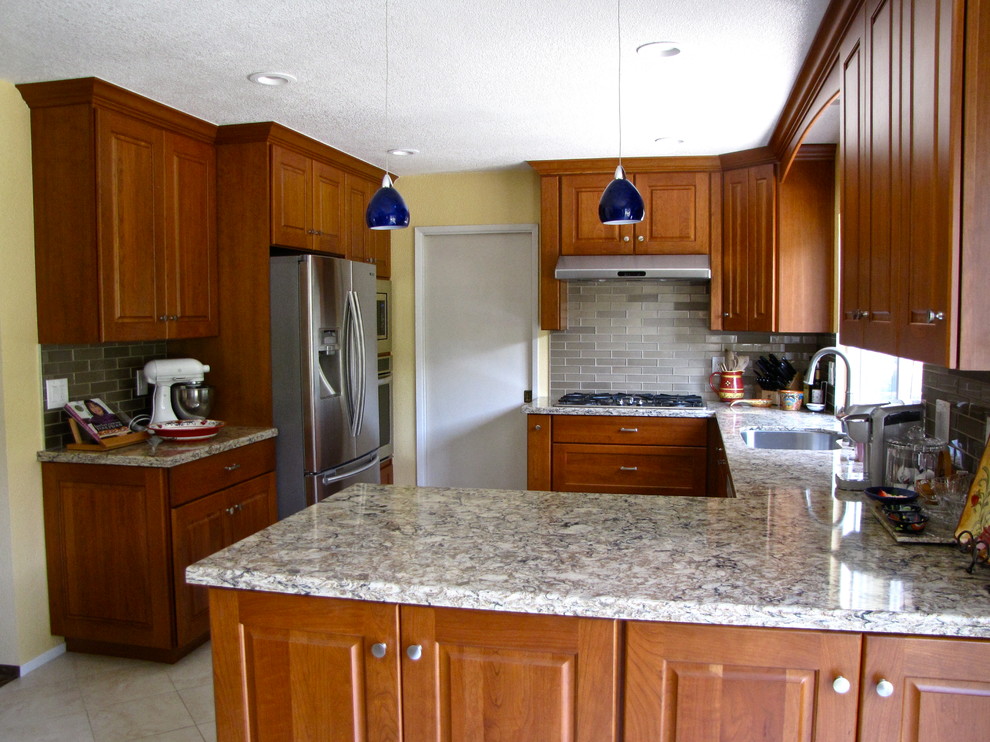 Photo of a transitional l-shaped open plan kitchen in San Francisco with an undermount sink, recessed-panel cabinets, medium wood cabinets, granite benchtops, metallic splashback, cement tile splashback, stainless steel appliances, ceramic floors and a peninsula.