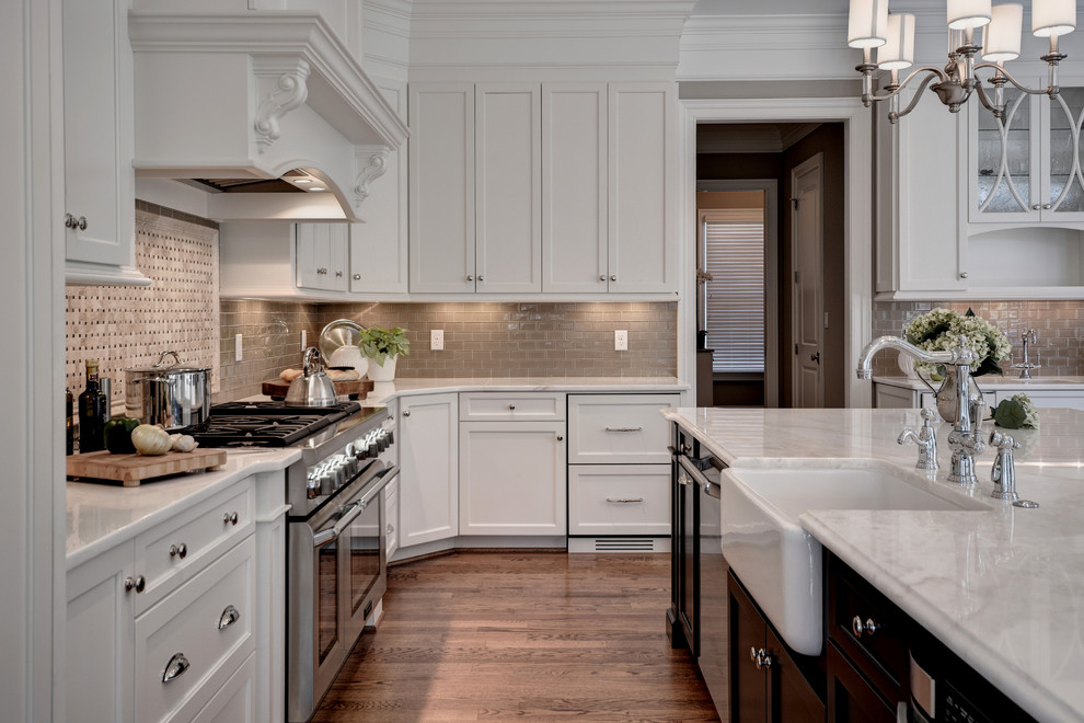 Inspiration for an expansive transitional l-shaped kitchen in Other with a farmhouse sink, shaker cabinets, white cabinets, marble benchtops, beige splashback, glass tile splashback, stainless steel appliances, medium hardwood floors, with island and brown floor.