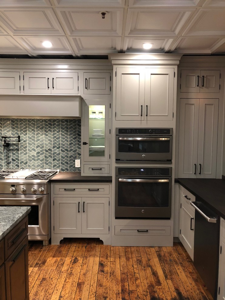 This is an example of a large arts and crafts l-shaped kitchen pantry in New York with an undermount sink, flat-panel cabinets, grey cabinets, wood benchtops, green splashback, porcelain splashback, stainless steel appliances, medium hardwood floors, with island, brown floor and brown benchtop.