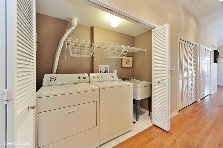 This is an example of a mid-sized transitional single-wall laundry cupboard in Chicago with an utility sink, brown walls, ceramic floors and a side-by-side washer and dryer.