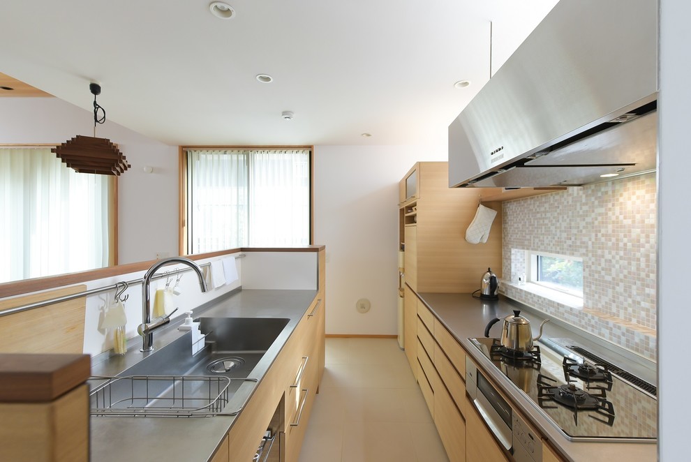 Photo of a contemporary galley kitchen in Other with an integrated sink, flat-panel cabinets, light wood cabinets, stainless steel benchtops, multi-coloured splashback, mosaic tile splashback and beige floor.