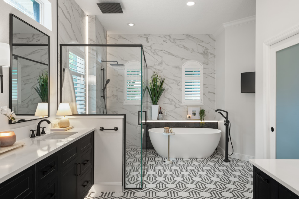 Example of a mid-sized transitional master white tile and porcelain tile mosaic tile floor, multicolored floor and double-sink freestanding bathtub design in Orlando with raised-panel cabinets, black cabinets, a one-piece toilet, white walls, a drop-in sink, quartz countertops, a hinged shower door, white countertops, a niche and a floating vanity