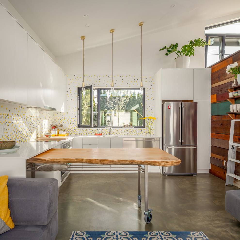 Photo of a large contemporary l-shaped eat-in kitchen in Vancouver with flat-panel cabinets, white cabinets, mosaic tile splashback, stainless steel appliances, concrete floors, with island, grey floor, a single-bowl sink, quartz benchtops, multi-coloured splashback and white benchtop.