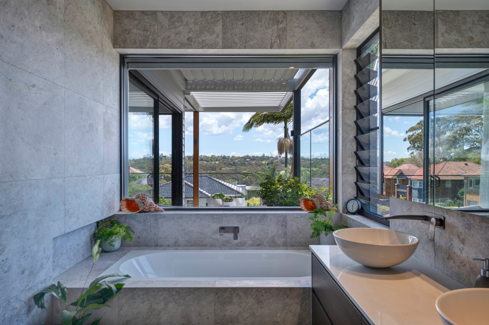 シドニーにある高級な中くらいなコンテンポラリースタイルのおしゃれなマスターバスルーム (濃色木目調キャビネット、ドロップイン型浴槽、石タイル、白い洗面カウンター、洗面台2つ、フローティング洗面台) の写真