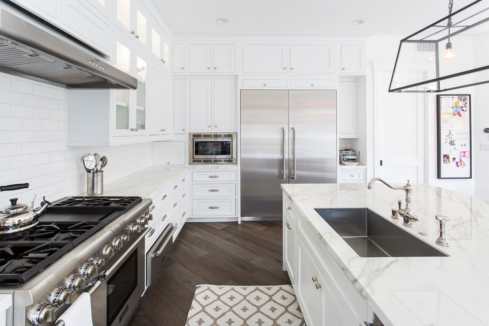 Beach style eat-in kitchen in Los Angeles with medium wood cabinets, white splashback, porcelain splashback, stainless steel appliances, medium hardwood floors, with island and brown floor.
