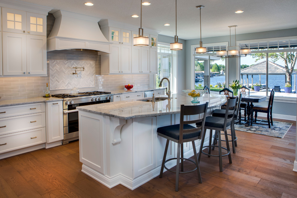 Inspiration for a mid-sized farmhouse l-shaped light wood floor eat-in kitchen remodel in Orlando with an undermount sink, shaker cabinets, white cabinets, granite countertops, gray backsplash, subway tile backsplash, stainless steel appliances and an island