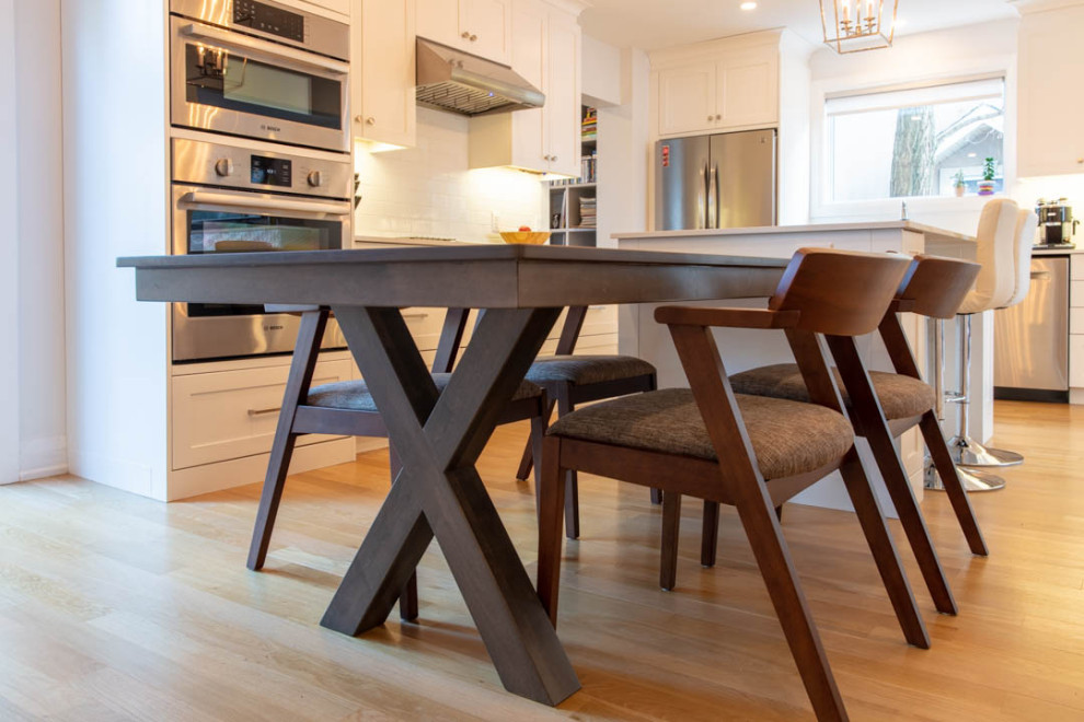 Inspiration for a large transitional l-shaped light wood floor eat-in kitchen remodel in Ottawa with a farmhouse sink, shaker cabinets, white cabinets, quartz countertops, white backsplash, porcelain backsplash, stainless steel appliances, an island and white countertops