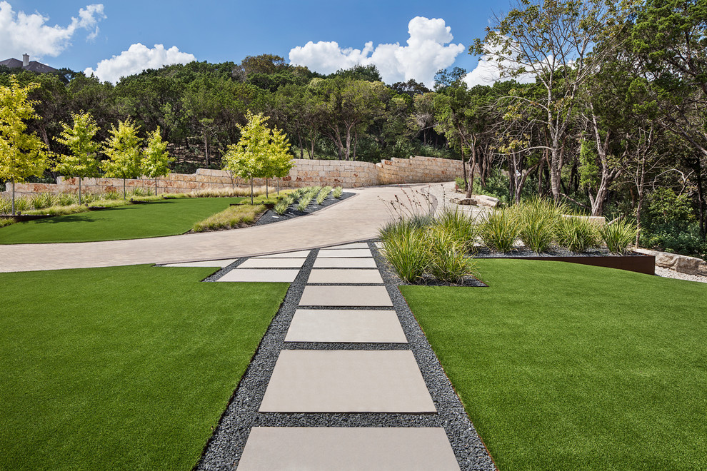This is an example of a large modern front yard full sun driveway for spring in Austin with a garden path and concrete pavers.