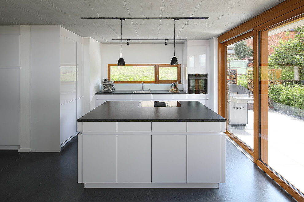 Mid-sized contemporary l-shaped open plan kitchen with a drop-in sink, flat-panel cabinets, white cabinets, black appliances, vinyl floors, with island, black floor, black benchtop and window splashback.