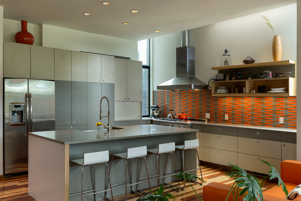 This is an example of a contemporary l-shaped kitchen in Kansas City with a farmhouse sink, flat-panel cabinets, grey cabinets, orange splashback, stainless steel appliances, medium hardwood floors and with island.