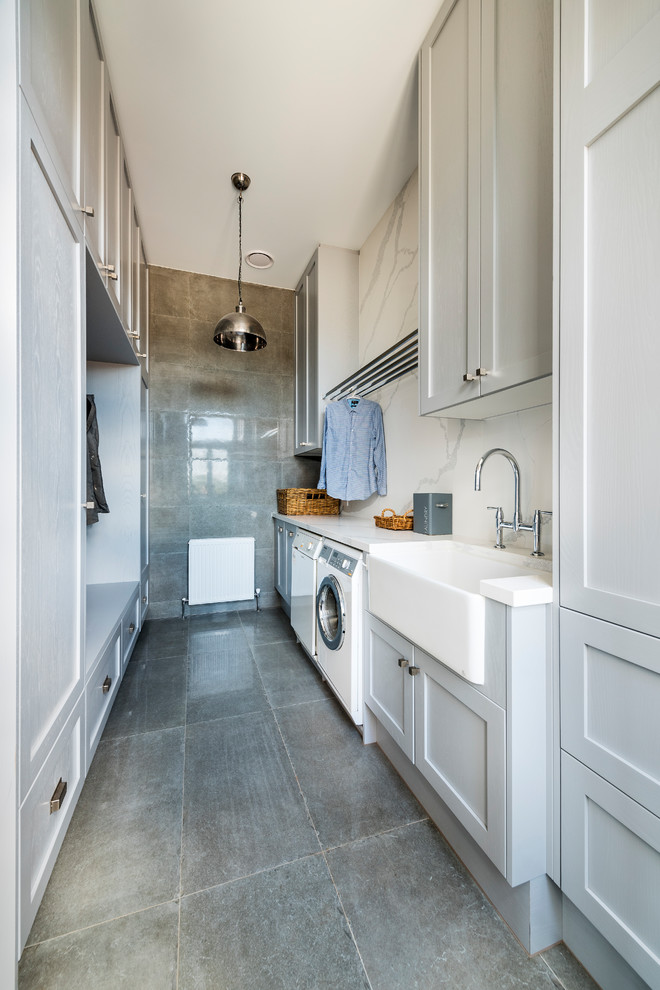 Photo of an expansive country galley utility room in Melbourne with a farmhouse sink, shaker cabinets, grey cabinets, quartz benchtops, concrete floors, grey floor, white benchtop, grey walls and a side-by-side washer and dryer.