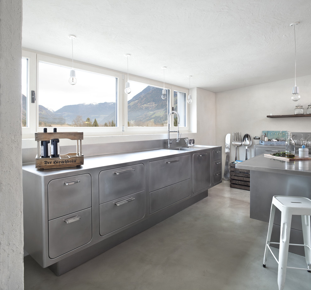 Design ideas for a large industrial kitchen in Venice with an integrated sink, flat-panel cabinets, stainless steel cabinets, stainless steel benchtops, concrete floors and with island.